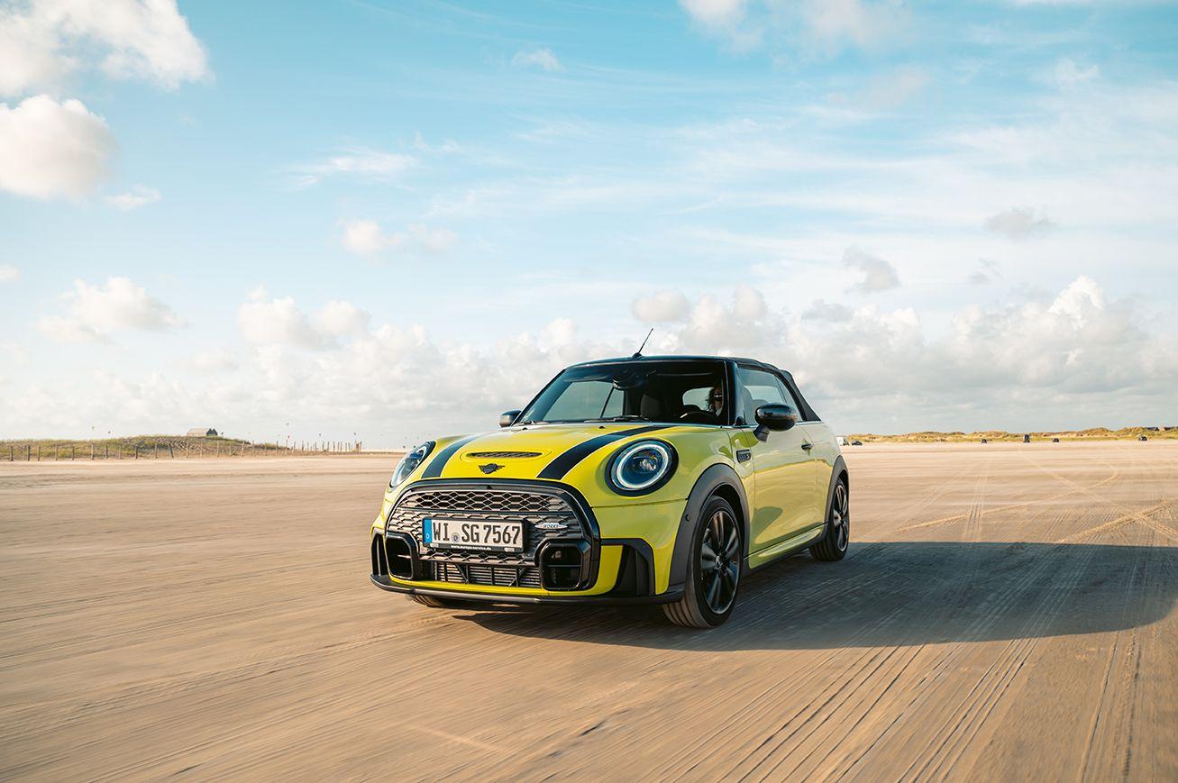 Gelber Mini Cooper fährt auf einem Sandstrand unter blauem Himmel.