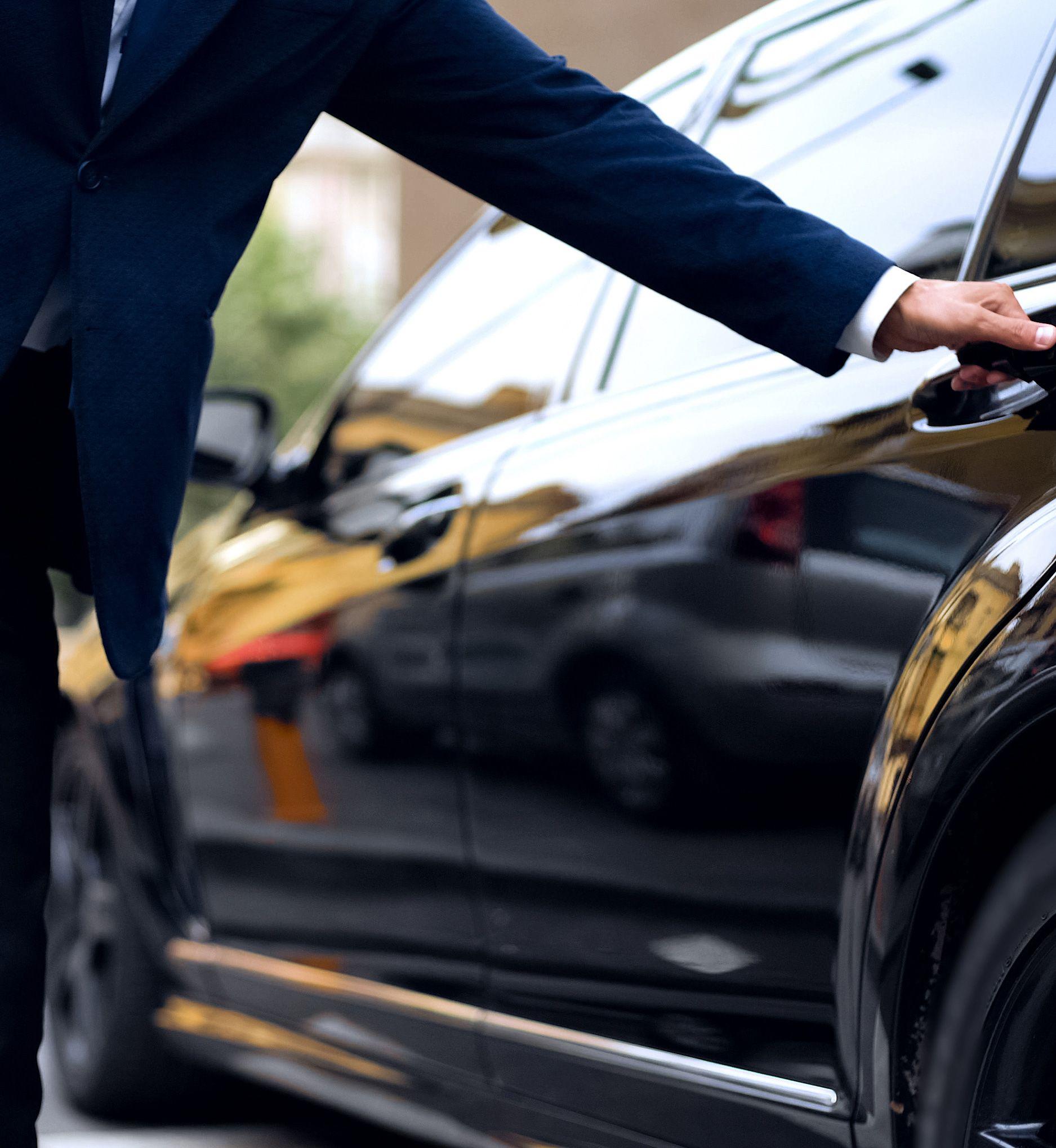 Eine Person öffnet die Tür eines schwarzen Autos.