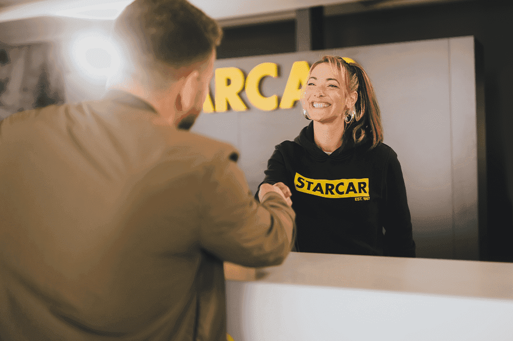Lächelnde STARCAR Mitarbeiterin schüttelt einem Kunden die Hand.