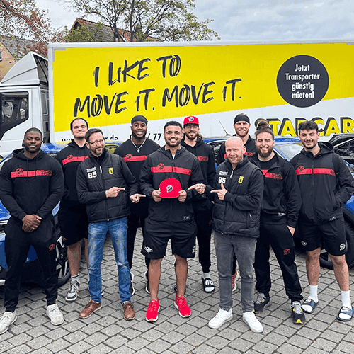 Gruppe von personen in Marken-Sportbekleidung vor einem Mietwagen.