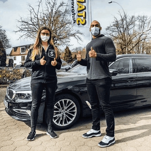 Zwei Personen geben Daumen hoch neben einem schwarzen BMW.