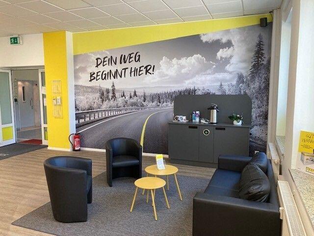 Starcar Autovermietung Station München-Nord Innenansicht: Wartebereich mit bequemen Sitzen und Straßenmotiv.