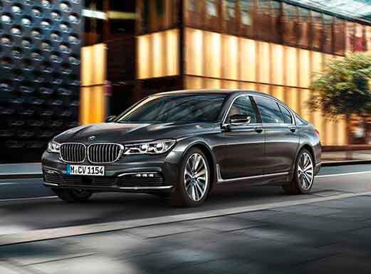 Dunkelgrauer 7er BMW fährt auf einer Stadtstraße.