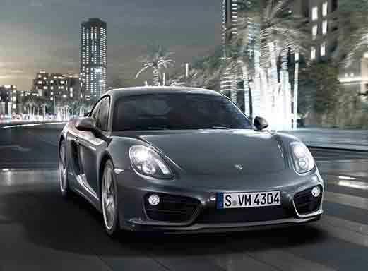 Silberner Porsche Cayman fährt nachts, beleuchtet von Stadtlichtern.
