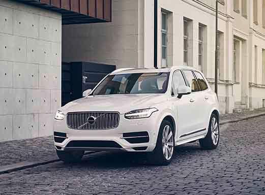 Weißer Volvo XC90 auf gepflasterter Straße neben einem Gebäude.