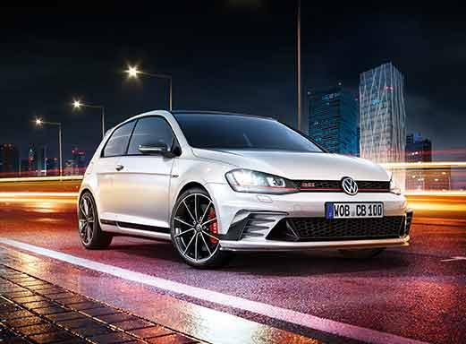 Weißer VW Golf GTI fährt nachts mit verschwommenen Stadtlichtern.