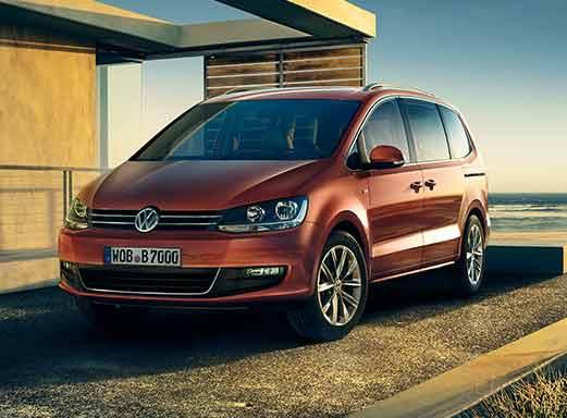 Roter VW Sharan Minibus geparkt in der Nähe eines Gebäudes und des Meeres.