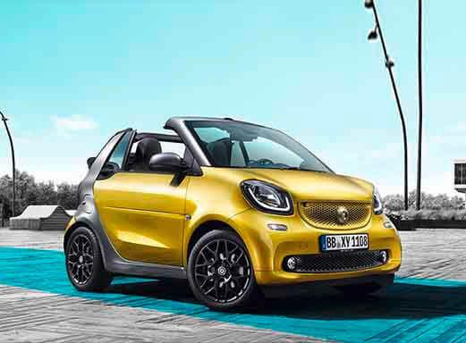 Gelbes Smart Fortwo Cabrio Mietwagen auf blauem Pflaster geparkt.