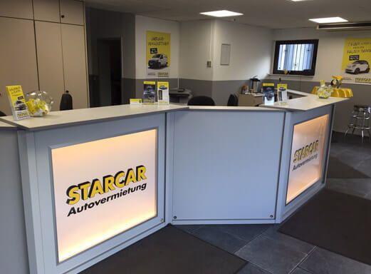 Innenansicht einer STARCAR Autovermietungsstation mit einer beleuchteten Rezeption.