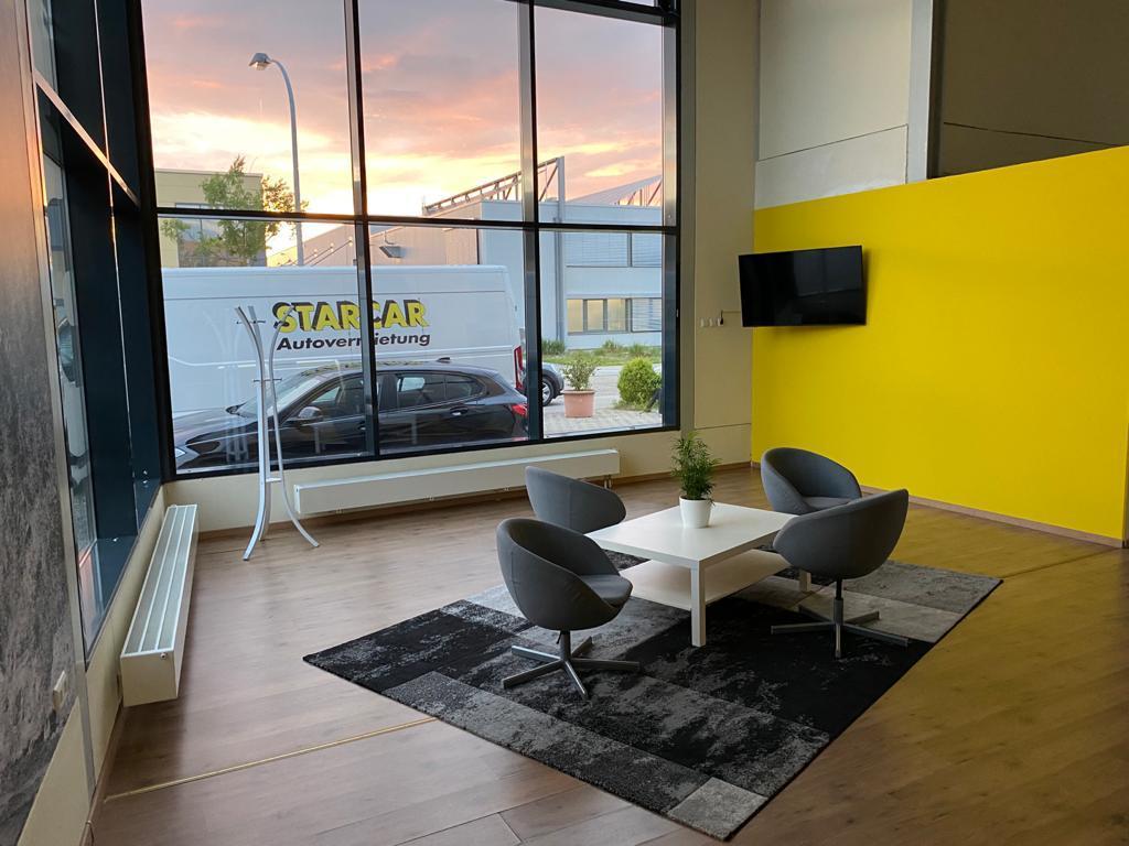 Innenansicht einer STARCAR Autovermietungsstation mit Sitzbereich und großen Fenstern.