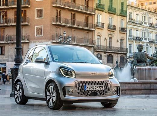 Silberner Smart EQ Elektro-Pkw, geparkt in der Nähe eines Brunnens auf einem Stadtplatz.