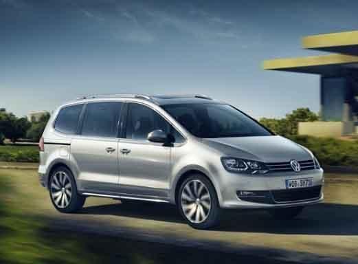 Silberner VW Sharan Minibus fährt auf einer sonnigen Straße.