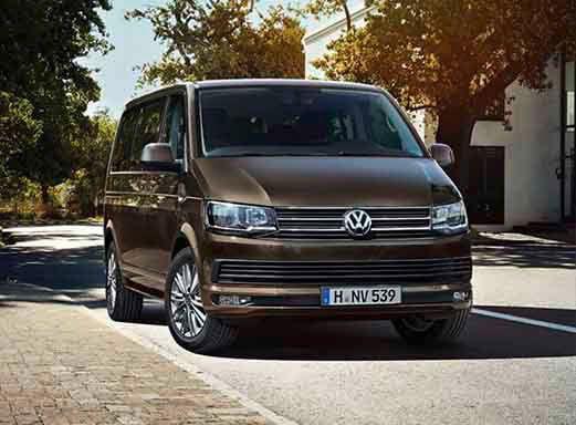 Brauner VW T6 Multivan Mietwagen auf einer sonnigen Straße.